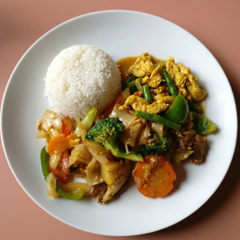 A white plate with rice, yellow curry chicken, and stir-fried vegetables.
