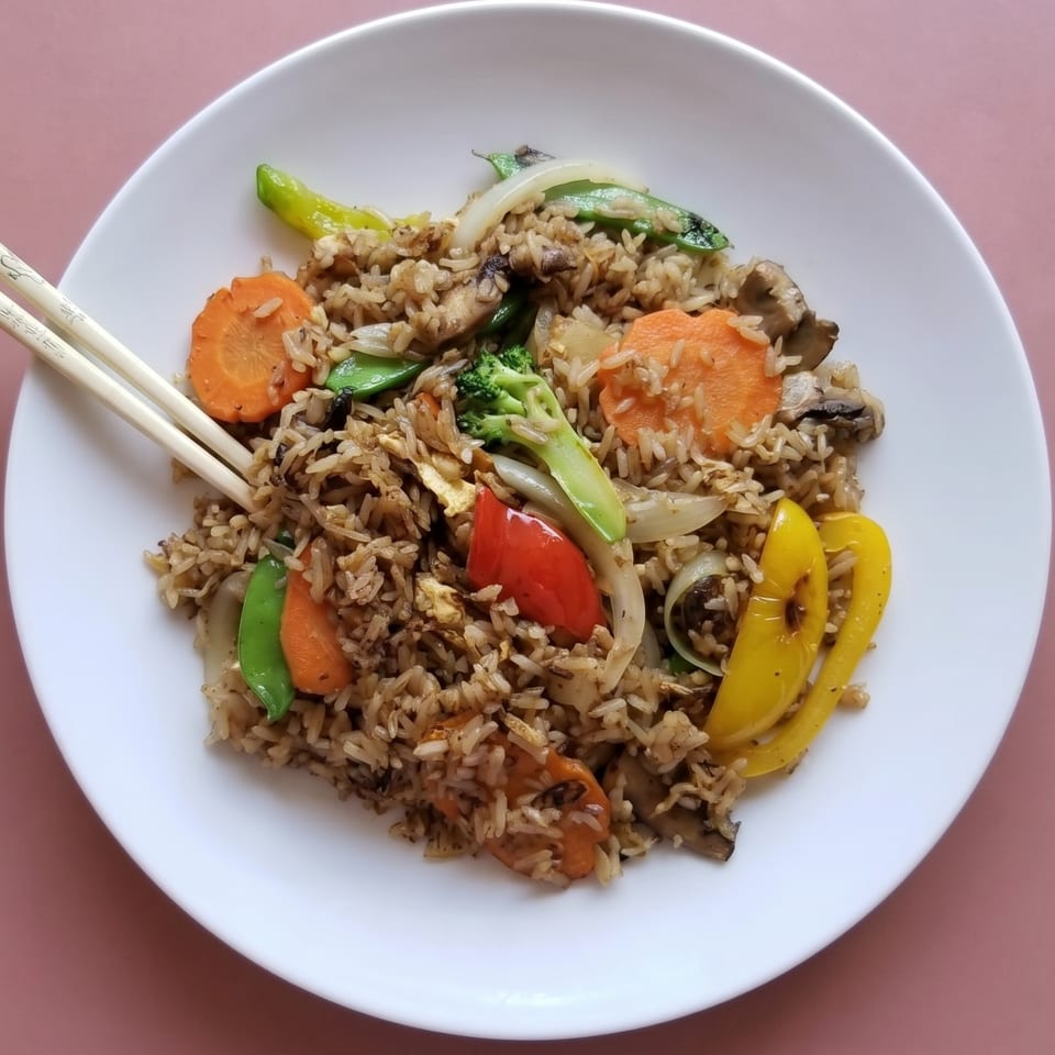 Vegetable fried rice with carrots, bell peppers, broccoli, and snap peas on a white plate with chopsticks.