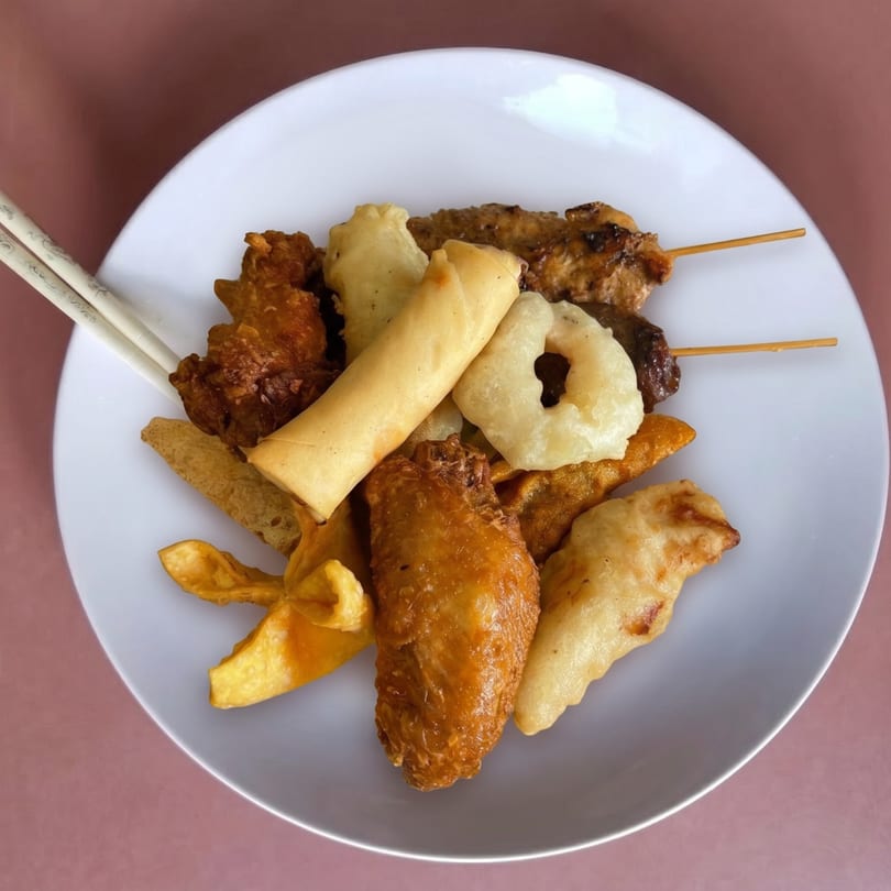 A white plate filled with various fried appetizers, including spring rolls, chicken wings, and skewers.