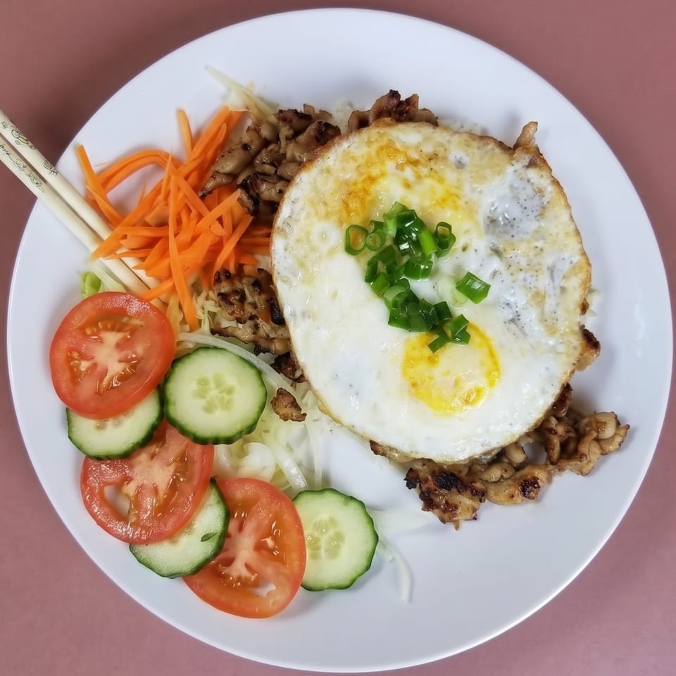 Vietnamese broken rice with grilled pork, a fried egg, shredded carrots, and sliced tomatoes and cucumbers.